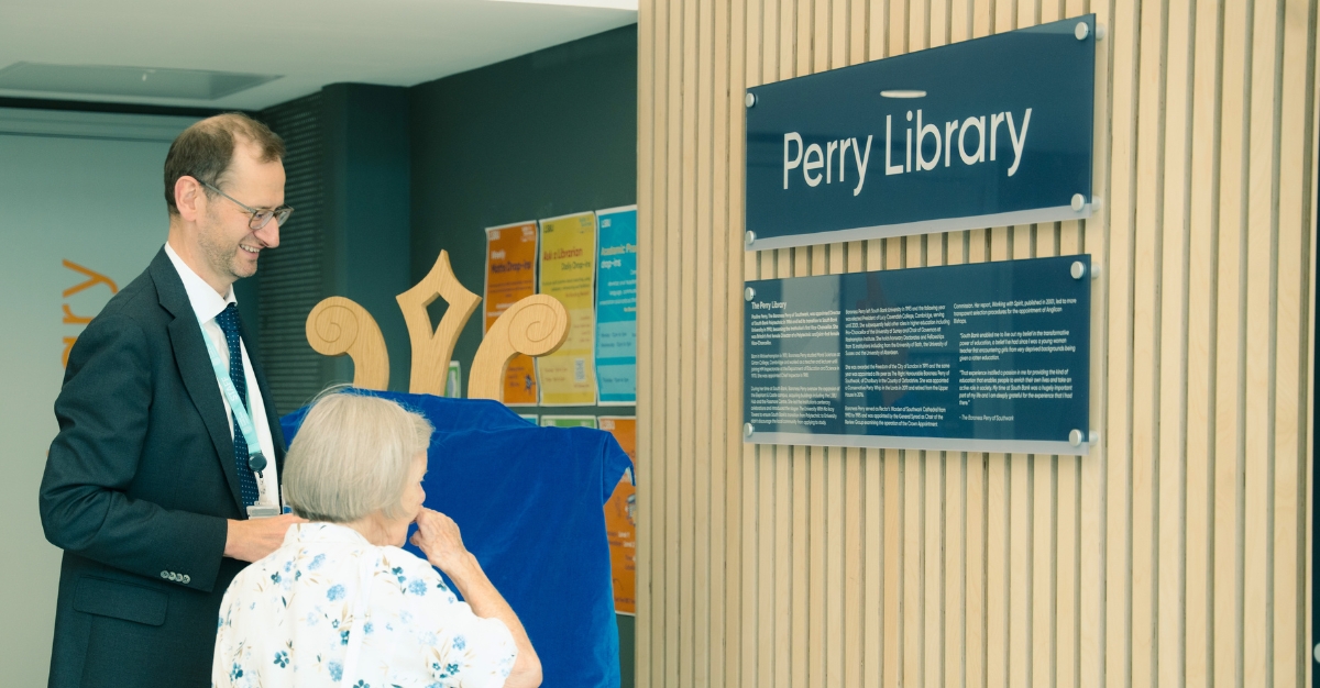 A man and a women stand looking at a sign on a wall that reads 'Perry Library