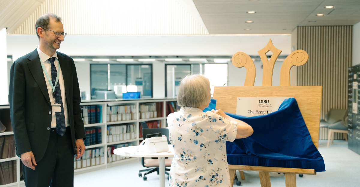 An elderly women removes a blue velvet curtain from a wooden board and plaque