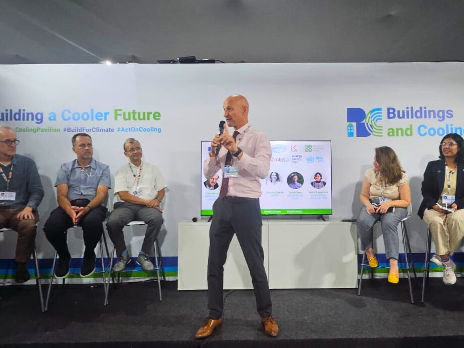 A man presenting in front of an panel of people sitting on a stage