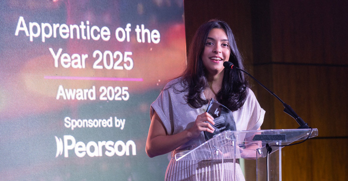 Isha Ahmed standing next to a screen and speaking into a microphone on a lecturn 