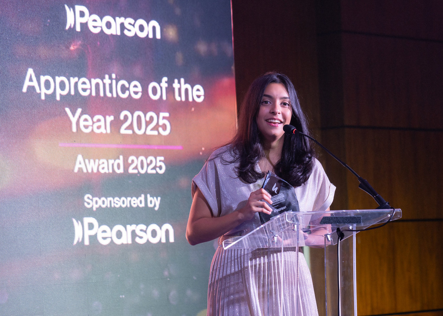Isha Ahmed standing next to a screen and speaking into a microphone on a lecturn 