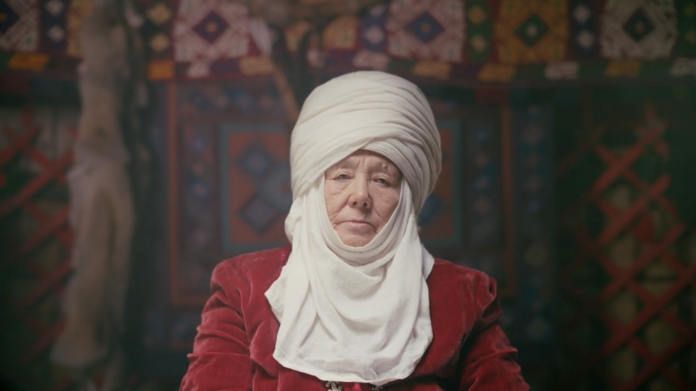 An elderly women in a headdress looks straight at the camera