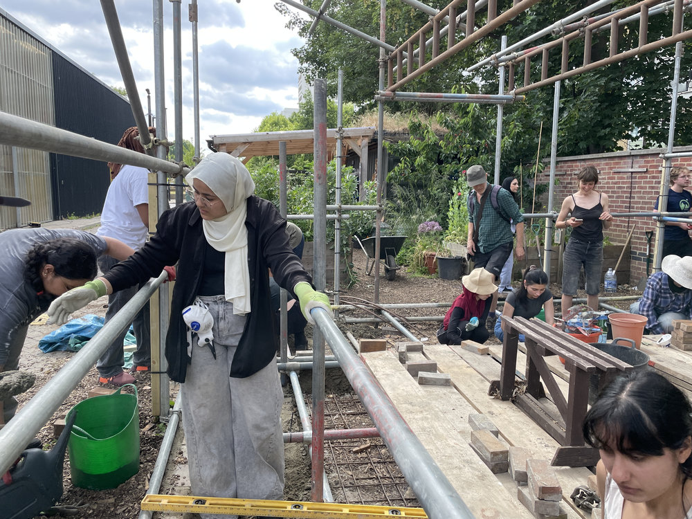 A team of people build scaffolding in an urban garden