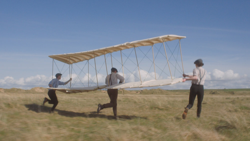 Three men run after an old fashioned wooden glider