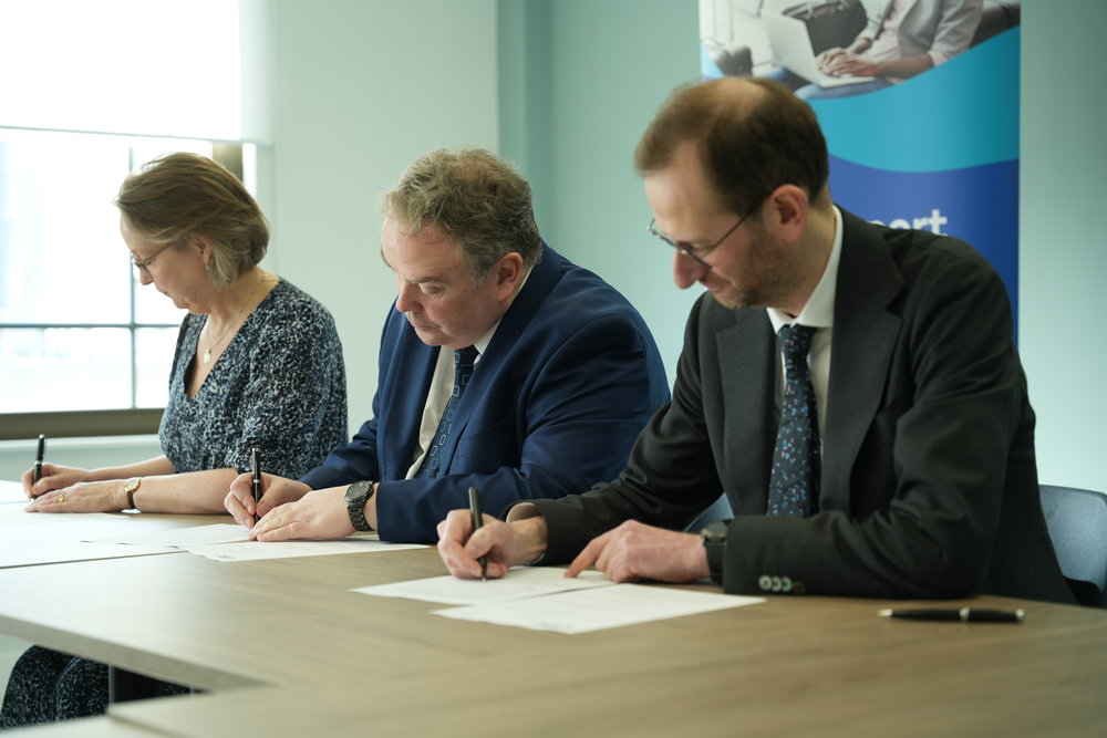 Three people sit at a desk signing papers each