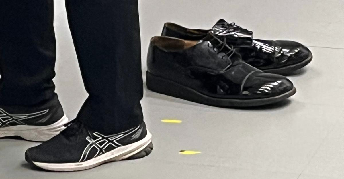 A pair of feet next to a pair of large black shoes