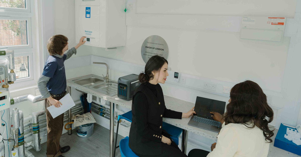 Three people working inside a white room, with one touching a heating boiler