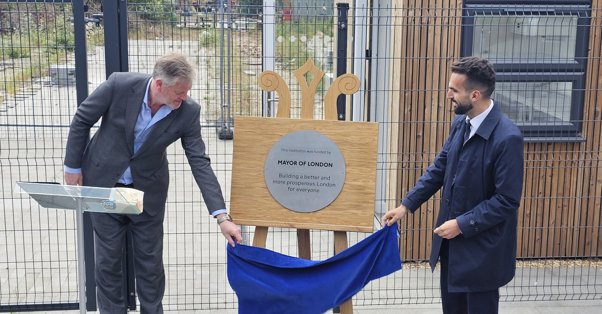 Two men unveiling a plaque on a wooden board