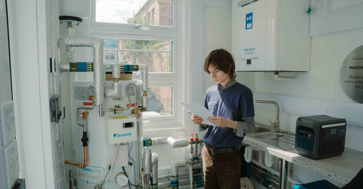A young man looks at a piece of paper as he stands next to a boiler